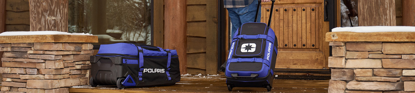 Ogio x Polaris-utrustningsväskor på verandan framför en timmerstuga i snö
